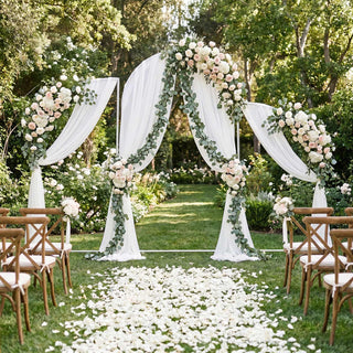 Elegant outdoor wedding arch with white drapes, greenery, and blush floral arrangements