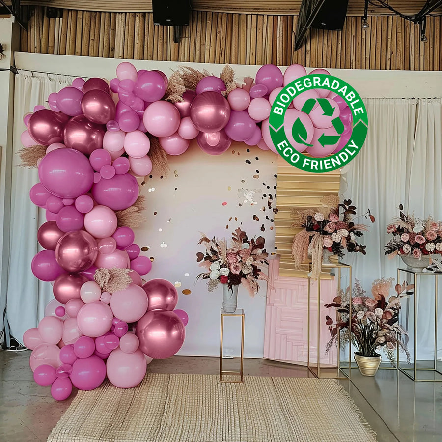 Pink balloon arch with floral arrangements and eco-friendly label.