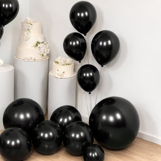 Black balloons in various sizes with white floral cake displays in the background.