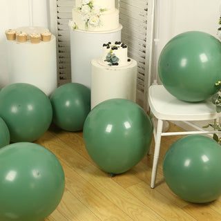 Green balloons scattered around a white chair and cake in a styled setting.