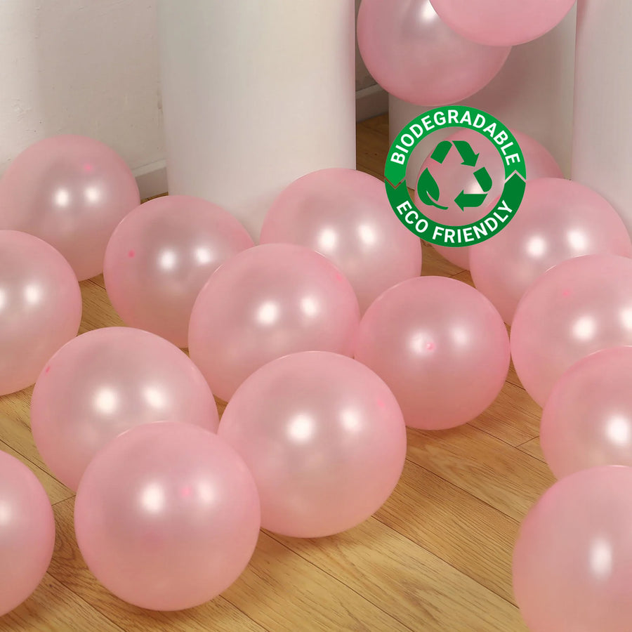 Pink biodegradable balloons scattered on a wooden floor with eco-friendly label.