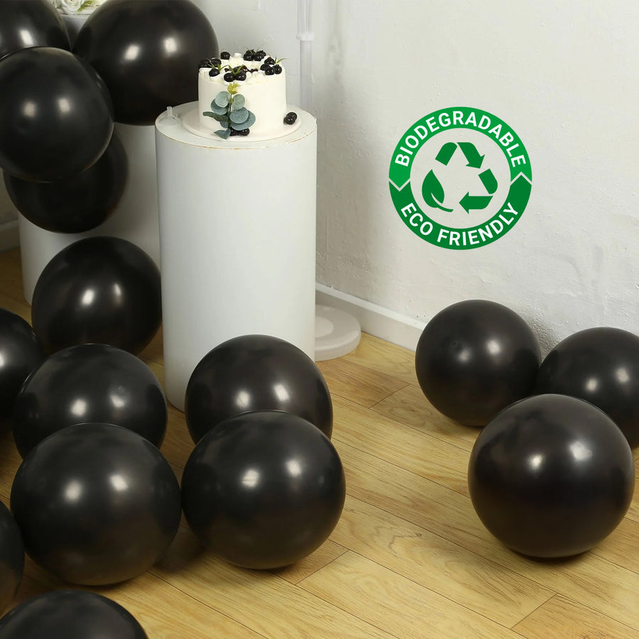 Black biodegradable balloons scattered on a wooden floor with a cake and eco-friendly logo.