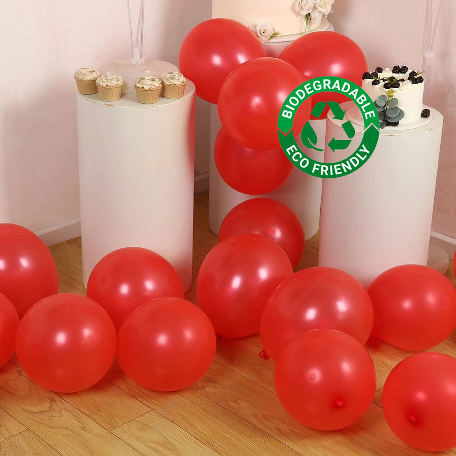 Red biodegradable balloons scattered on the floor with a cake and cupcakes nearby.