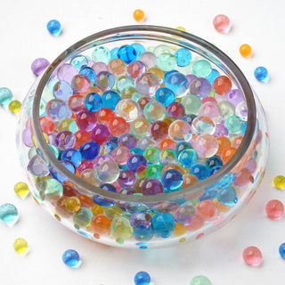 Colorful water beads in a glass bowl, with scattered beads around it.