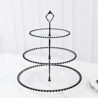 Black three-tiered serving stand with beaded edges on a marble surface.