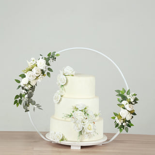 Three-tiered wedding cake adorned with white roses and greenery.