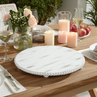 White wooden cake stand on a dining table with candles and flowers.