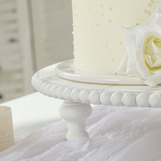 Elegant white cake adorned with pearls and a rose on a decorative stand.