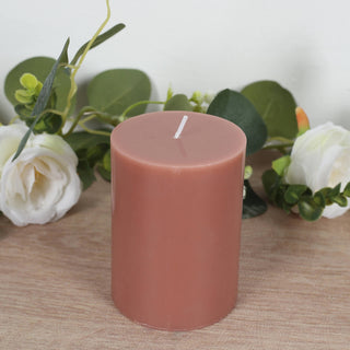 Pink pillar candle surrounded by greenery and flowers.