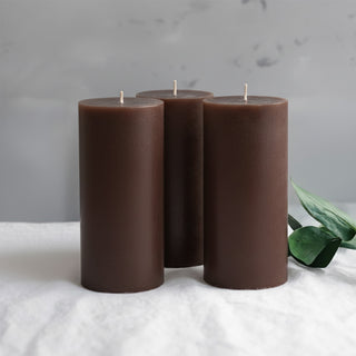 Set of three brown pillar candles with green foliage accents.