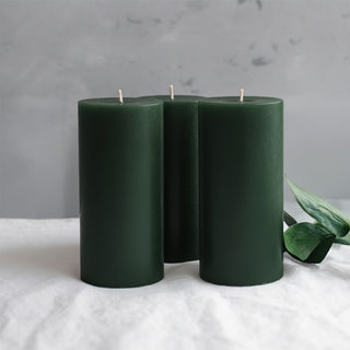 Green pillar candles arranged with greenery on a soft surface.