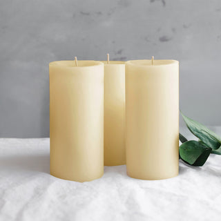 Three ivory candles with green leaves on a soft surface.