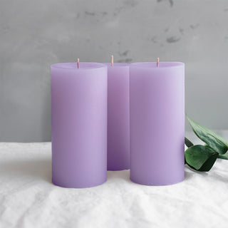 Three lavender candles with a subtle sheen and a green leaf on a soft surface.