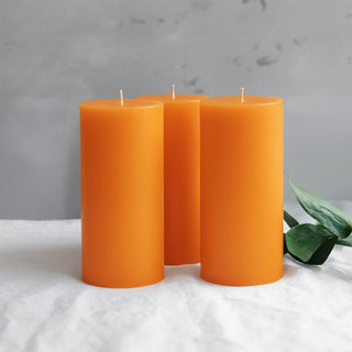 Three orange pillar candles with a green leaf accent on a light surface.