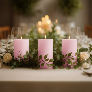Three pink candles surrounded by greenery and roses on a dining table.
