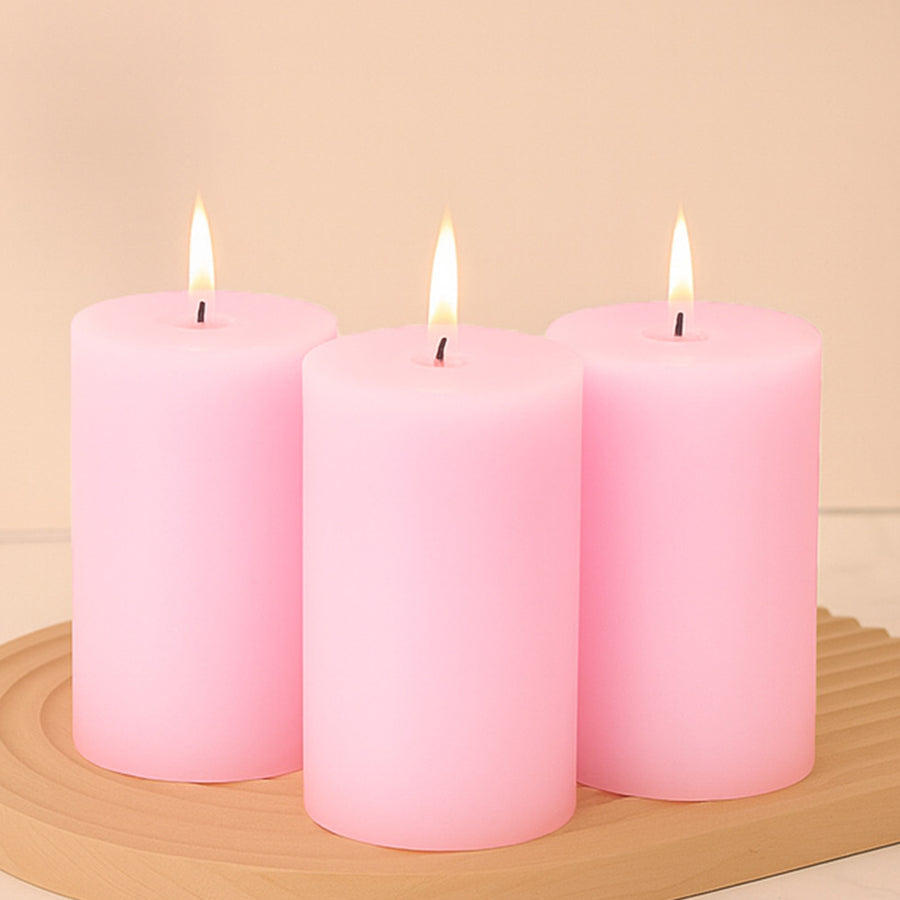 Three pink candles with flames on a wooden tray.