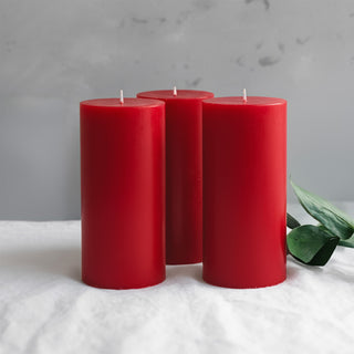 Three red candles with greenery on a light surface.