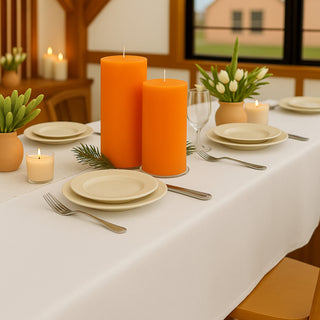 Orange candles on a beautifully set table with plates and plants.