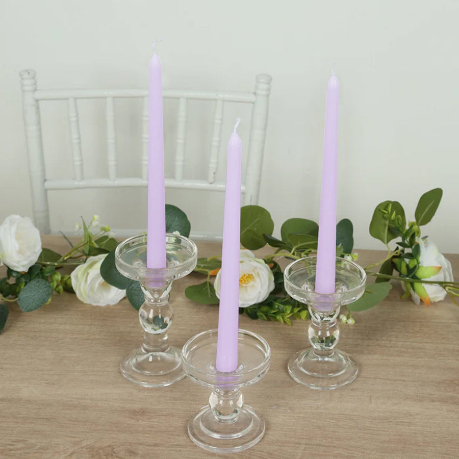 Purple taper candles in clear glass holders on a wooden table with floral accents.