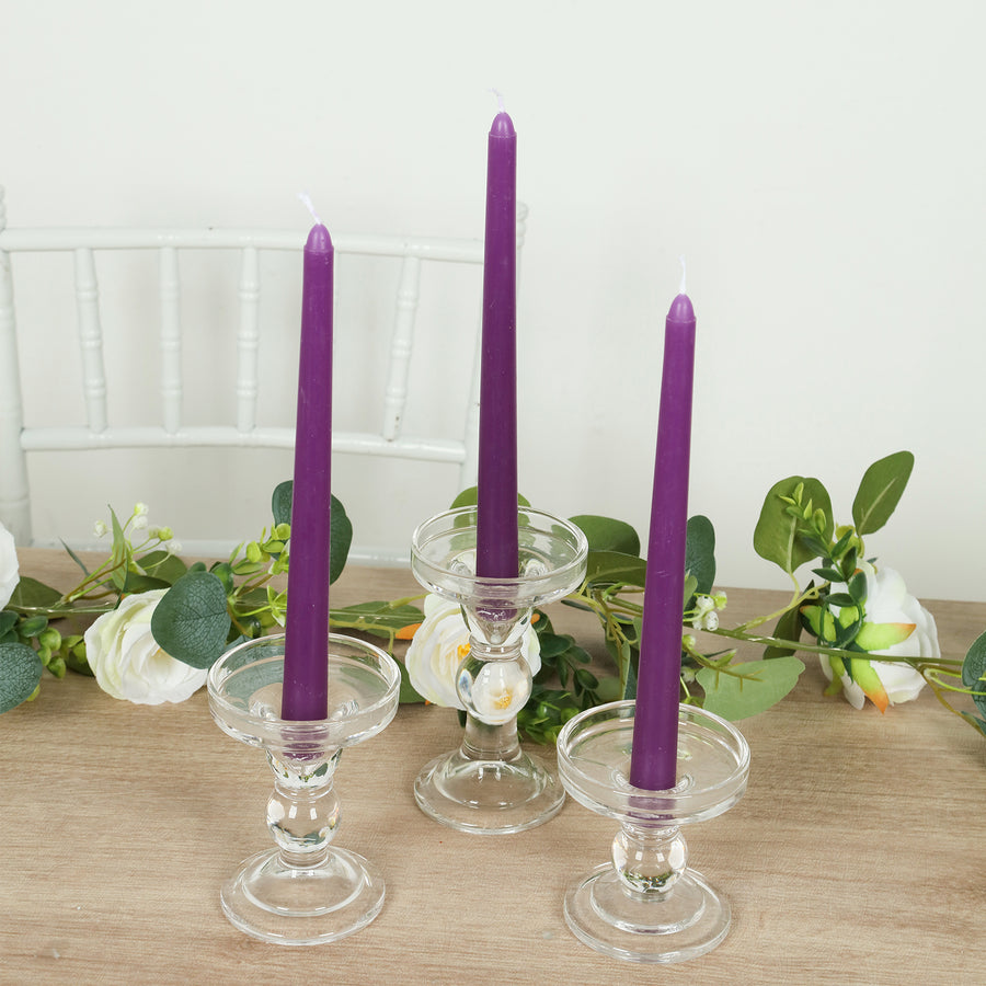 Purple candles in clear glass holders with greenery.
