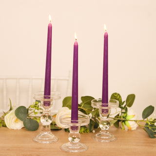 Purple taper candles in clear candle holders with greenery and flowers.