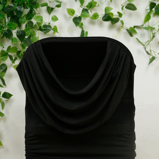 Black draped hooded dress on a mannequin against a green plant backdrop.