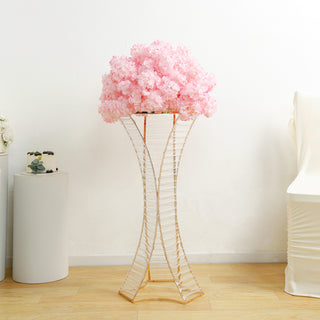 Pink floral arrangement in a stylish gold stand against a white background.