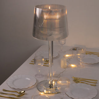 Elegant transparent lamp on a dining table with gold cutlery and soft lighting.