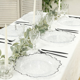 Elegant glass dinnerware set on a styled table with candles and greenery.