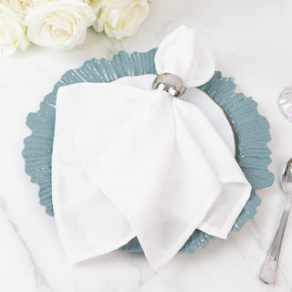 Elegant white napkin with silver ring on a teal plate, styled for dining.