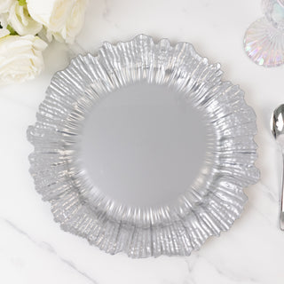Silver ruffled edge plate on a marble surface with flowers and glassware.