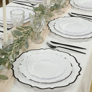 Elegant dining table set with white plates, glassware, and greenery accents.