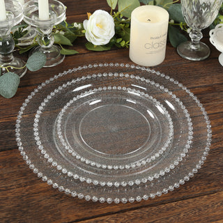 Elegant clear glass plates with beaded edges, stacked on a wooden table.