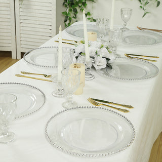 Elegant dining table set with clear plates and glassware, adorned with candles and flowers.
