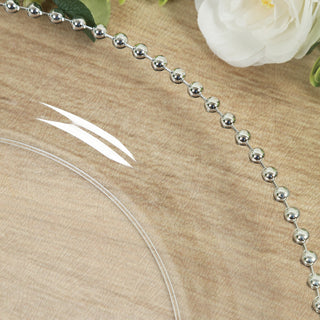 Clear glass plate with silver beaded rim on a textured surface.