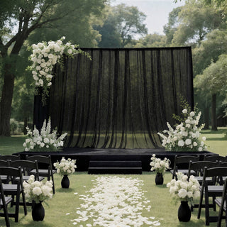 Outdoor wedding ceremony setup with black drapery and white floral arch
