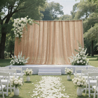 Outdoor wedding ceremony setup with white flowers, chairs, and gold draped backdrop