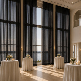 Elegant lakeside event hall with tall black drapes, candles, and white floral tables