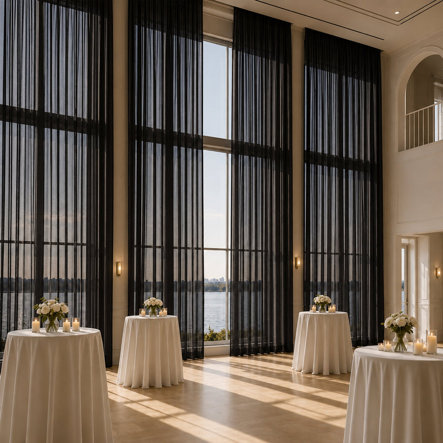 Elegant lakeside event hall with tall black drapes, candles, and white floral tables