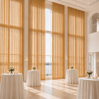 Elegant waterfront wedding reception with tall gold drapes and floral cocktail tables