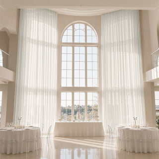 Elegant white wedding reception with tall arched windows and sheer curtains
