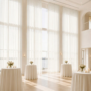 Elegant white wedding reception with tall sheer curtains and floral tables for events