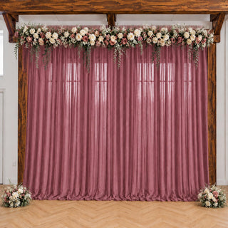 Pink wedding backdrop with floral garland and sheer drapes under wooden beams