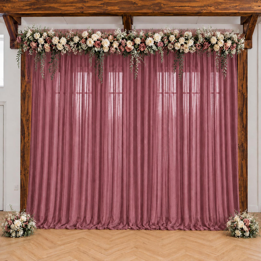 Pink wedding backdrop with floral garland and sheer drapes under wooden beams