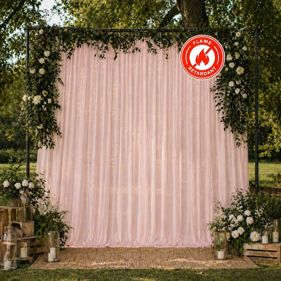 Outdoor wedding backdrop with blush drapes, greenery, and flame retardant sign