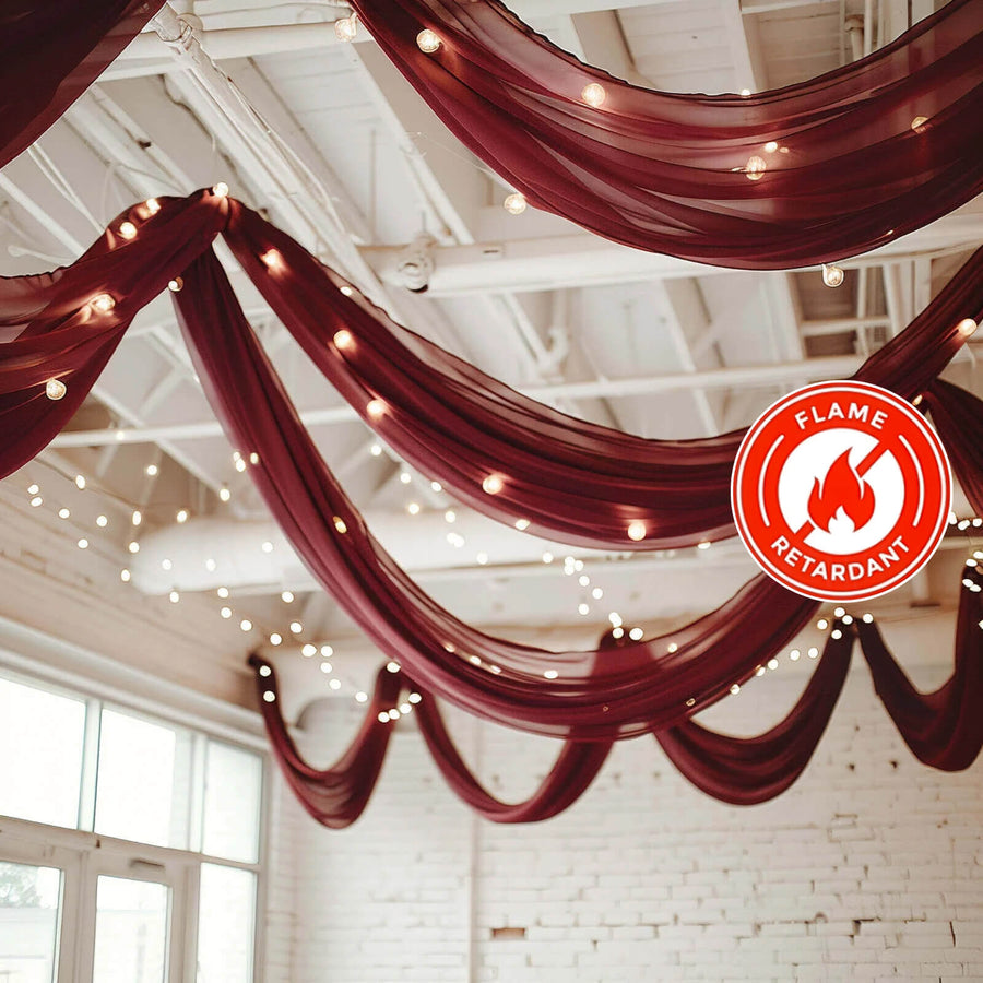 Burgundy drapery with fairy lights in a decorated venue, featuring flame retardant label.
