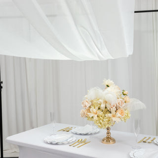 Elegant floral centerpiece on a dining table with white drapery backdrop.