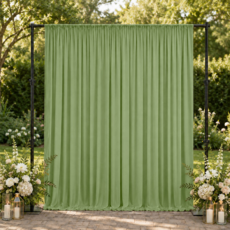 Green outdoor event backdrop with floral arrangements and candle lanterns