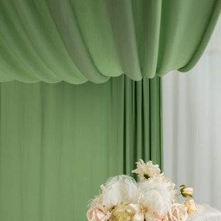 Green draped fabric backdrop with floral arrangement in front.
