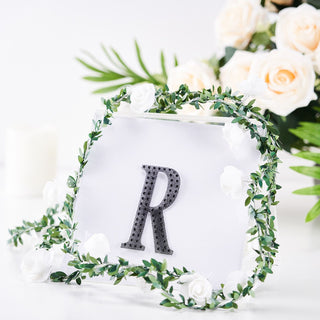 Decorative letter "R" framed with floral accents on a clear background.